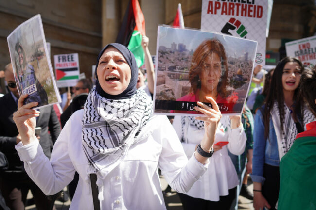 Manifestation à Londres (14 mai 2022) où l'on voit une femme en foulard avec keffieh portant une photo de la journaliste d'al-Jazeera Shireen Abu Aqleh